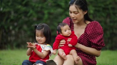 mother playing with baby and toddler girl while sitting on the grass field