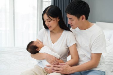 parent (mother and father) holding and consoling newborn baby to sleeping on a bed