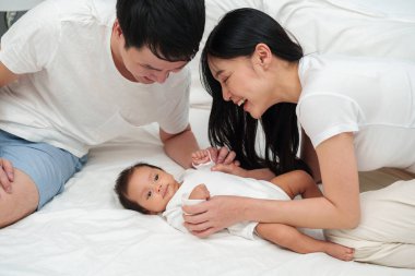 happy parents (father and mother) talking and playing with baby on a bed