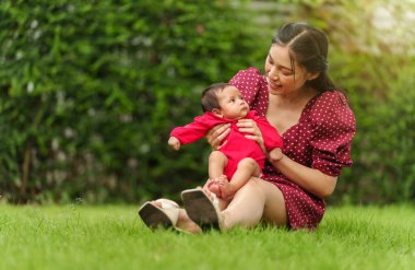 mother holding and playing with her baby newborn while sitting on the grass field