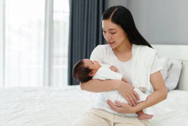 Anne yeni doğmuş bebeğini kucağına alıp yatakta konuşuyor.