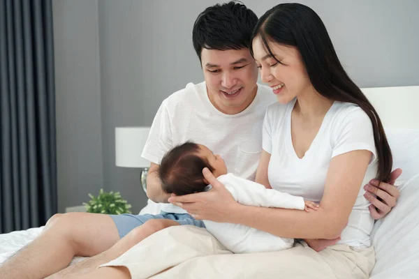 happy parents (father and mother) talking and playing with baby on a bed