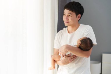 father holding newborn baby while looking out of the window