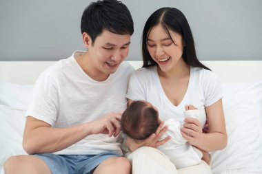 happy parents (father and mother) talking and playing with baby on a bed