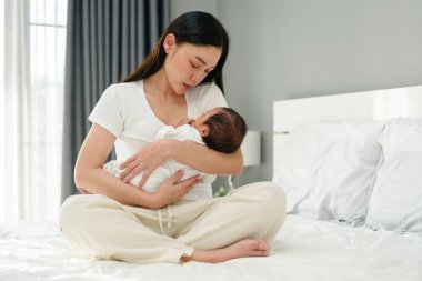 Anne kucağında yeni doğmuş bebeğini yatakta uyuması için teselli ediyor.