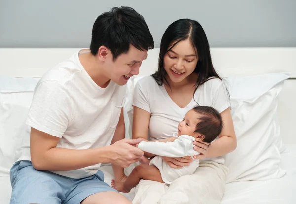 happy parents (father and mother) talking and playing with baby on a bed
