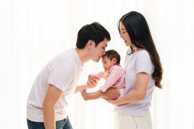 Baba yeni doğmuş bebeği öperken anne onu beyaz pencere arkasında tutuyor. Mutlu aile kavramı