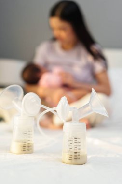 Anne sütü, anne sütü emziren yeni doğan bebeklerin arka planına sahip bir yatağın üzerine kurulmuş elektrikli meme pompalama şişelerinin içinde.