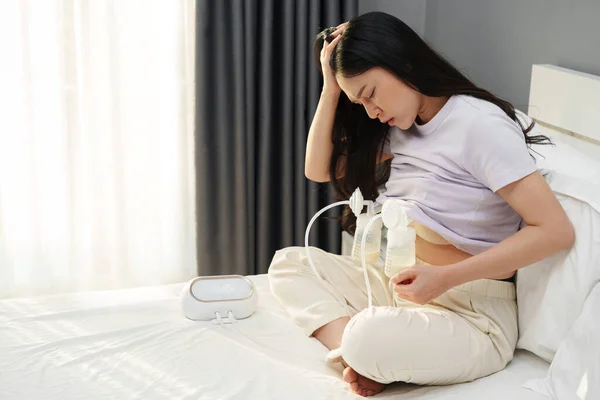 stressed mother using breast pump machine to pumping milk for her newborn baby on a bed