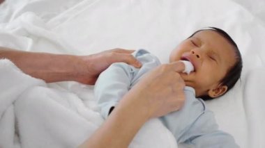 Anne yeni doğmuş bebek ağzını temizlemek için parmağını kullanıyor. Yatağın üzerinde temiz gazlı bez kullanıyor.