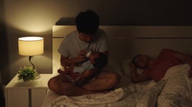 Stresli baba, karısı geceleri yatakta uyurken ağlayan bebeğini süt şişesiyle beslemeye çalışıyor.