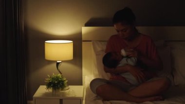 Stresli anne gece yatakta ağlayan bebeğini süt şişesiyle beslemeye çalışıyor.