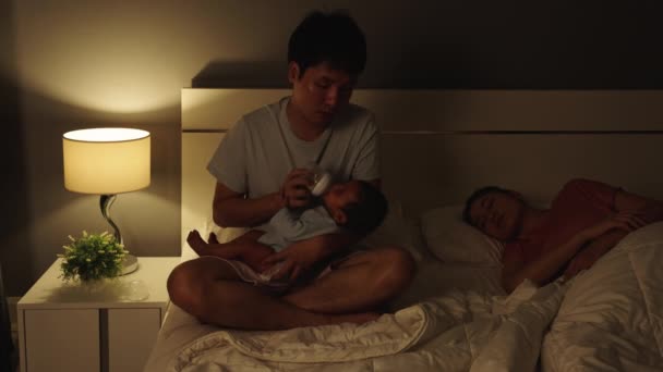 Álmos Fáradt Apa Cumisüveggel Eteti Újszülöttet Miközben Felesége Ágyon Alszik — Stock videók