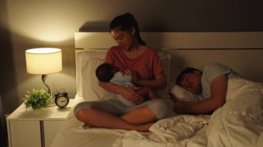 Annesi yeni doğan bebeği emzirirken kocası geceleri yatakta uyuyor.