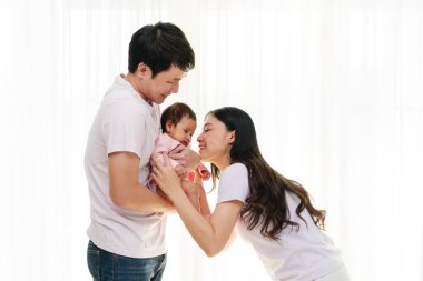 Neşeli bir anne ve baba, beyaz pencere arkasında yeni doğmuş bir bebekle sarılıp oynuyorlar. Mutlu aile kavramı