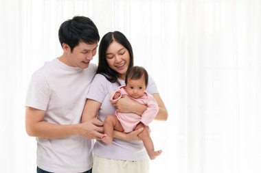 Neşeli bir anne ve baba, yeni doğmuş bebeği beyaz pencere arkasında tutuyorlar. Mutlu aile kavramı