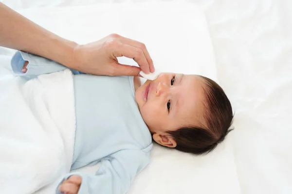 stock image mother cleaning and wiping newborn baby face with cotton pad on a bed