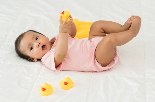 赤ちゃんはベッドの上で黄色いゴム製のアヒルのおもちゃで遊んでいます — ストック写真