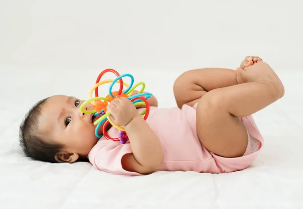 infant baby biting colorful rubber bites toy on a bed