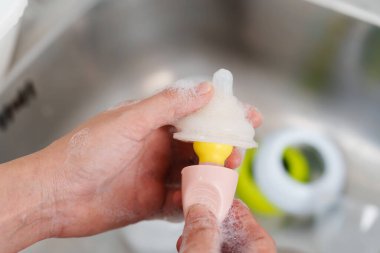 Anne eli bebeği yıkıyor plastik meme ucu süt şişesi.