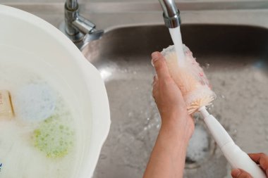 Anne eli bebek için plastik süt şişesini yıkıyor.