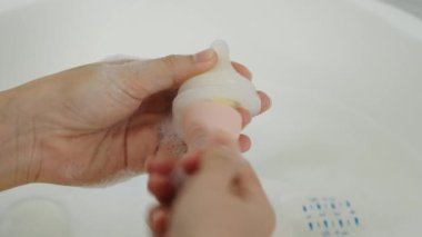 Anne eli bebeği yıkıyor plastik meme ucu süt şişesi.