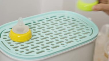 Anne eli buharlı sterilizatöre süt şişesi atıyor.