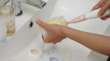 Anne eli bebek için plastik süt şişesini yıkıyor.