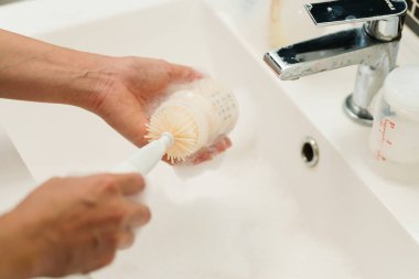 Anne eli bebek için plastik süt şişesini yıkıyor.