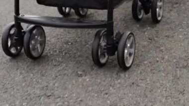 Bebek arabasının tekerleğini kapat. Yolda yürüyen ve iten bir kadın var.