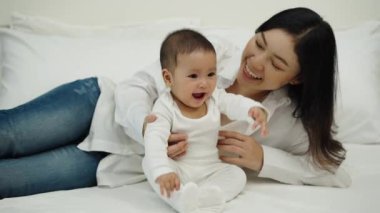 Mutlu anne ve bebeği bir yatakta oturup oynuyorlar.