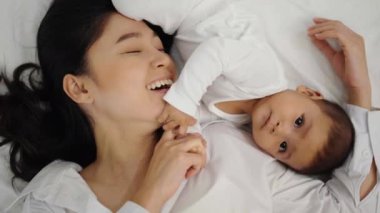 Mutlu anne yalan söylüyor ve bebeğiyle yatakta oynuyor.