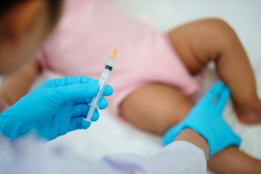 Doktor şırıngayı tutuyor ve aşıyı hazırlıyor. Bebek bacağına iğne yapıyor.