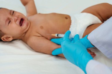 Doktor şırıngayı tutuyor ve aşıyı hazırlıyor. Ağlayan bebek koluna iğne yapıyor.