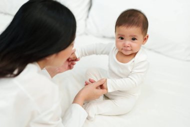 Mutlu anne ve bebeği bir yatakta oturup oynuyorlar.