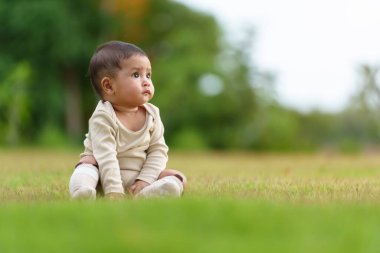 Parktaki yeşil çimlerin üzerinde oturan bir bebek.