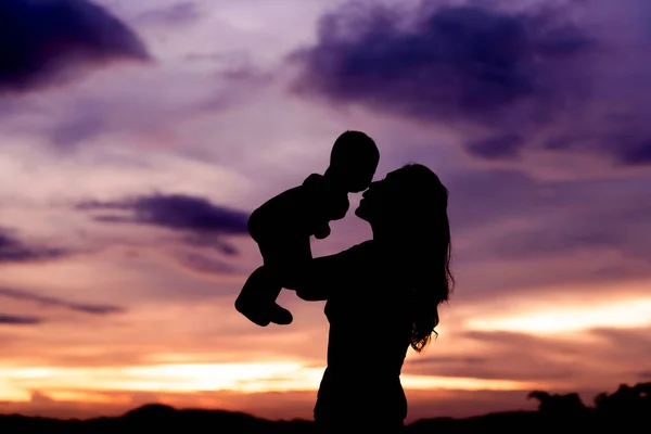 सूर्योदयाच्या वेळी तिच्या बाळाबरोबर आई धारण आणि चुंबन घेण्याची कल्पना स्टॉक पिक्चर
