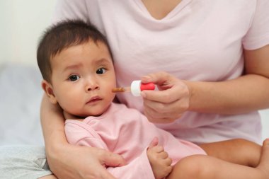 Anne, hasta bebeğe bir damlacıkla sıvı ilaç veriyor.