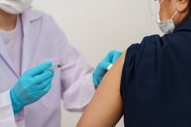 Doktor elinde şırıngayla hastaya tıbbi maske takmadan önce pamuk kullanıyor. Covid-19 veya koronavirüs aşısı