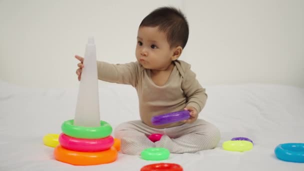 Baby Spielt Pyramidenspielzeug Mit Farbigen Ringen Auf Einem Bett — Stockvideo