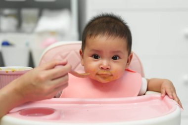 Anne, bebeğine yemek yediriyor. Evde kaşıkla yiyor.
