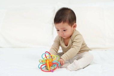 Bebek renkli lastik ısırıklarıyla oynuyor. Oyuncak yatakta.