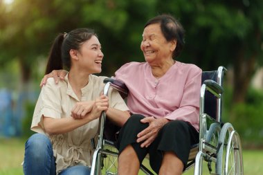 Mutlu genç torun parkta tekerlekli sandalyedeki yaşlı kadınla konuşuyor.