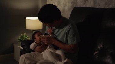 Baba, gece bebek için süt şişesini oturma odasındaki kanepede besliyor.