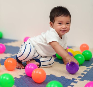Mutlu bebek oyun parkında renkli plastik toplarla oynuyor.
