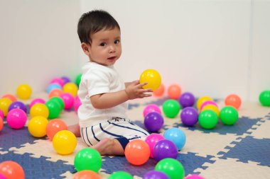 Mutlu bebek oyun parkında renkli plastik toplarla oynuyor.