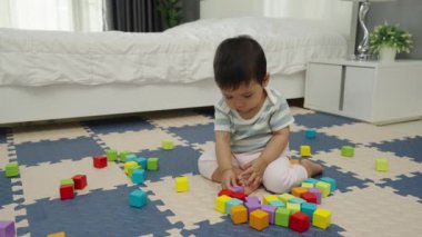 Mutlu bebek bebek yatak odasındaki yapboz minderinde tahta blok oyuncağı oynuyor.
