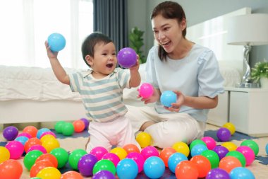 Mutlu bebek bebek, annesiyle renkli plastik toplar oynuyor. Yatak odasında yapboz minderiyle.