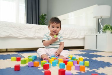Mutlu bebek bebek yatak odasındaki yapboz minderinde tahta blok oyuncağı oynuyor.