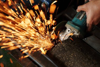 İşçi, metali öğütmek için açı öğütücü kullanıyor.